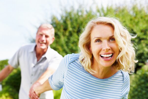 Cheerful woman holding hand of a senior man against sky